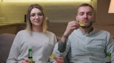 Erkek ve kız birlikte bira içip patates cipsi yiyorlar. TV dizileri ya da TV dizileri için aile gösterimi. Genç evli çift akşam evde dinleniyor, evdeki kanepede oturup televizyon izliyor..