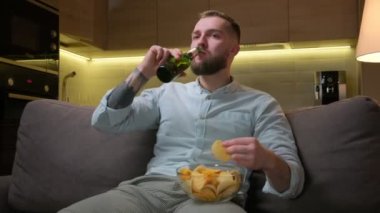 Tıraşsız bir adam geceyi evde televizyon izleyerek, alkollü bira içerek ve patates cipsi yiyerek geçirir. Televizyon izlemek, evdeki kanepede dinlenmek, spor kanalı ya da film izlemek..
