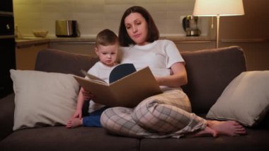 Ebeveynler çocuklarına okuldan önce okumayı, uzaktan öğrenmeyi, çocuk gelişimi kavramını öğretir. Hamile bir anne, sevgili sarışın çocuğuna kitap okurken akşamları oturma odasında kanepede oturuyor..