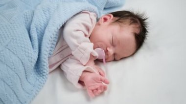 Krem rengi tulumlu yeni doğmuş bebek, mavi battaniyeyle kaplı yatakta huzur içinde uyuyor ve emzik emiyor. Çocuk uykusunda hırıldıyor, ağlıyor. Çocuk koruma ve çocuk.