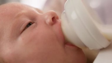  Portre bebek sulandırılmış süt tozu içiyor. Beyaz yeni doğmuş bebek emzik yoluyla küçük plastik bebek şişesinden anne sütü içiyor. Annelik ve çocukluk kavramı. Görüntüleri kapat.
