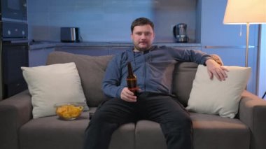 Adam TV 'deki eğlence programlarını izlemeye, alkol içmeye ve yemek yemeye odaklanmış. Geceleri traşsız bir adam karanlık bir salonda oturur televizyon izler, patates cipsi yer ve bira içer..