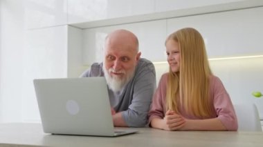 Yaşlı, gri saçlı büyükbaba ve torunu bilgisayarın karşı tarafında oturuyorlar ve video bağlantısıyla iletişim kuruyorlar. Video iletişimi yoluyla aile içi iletişim.