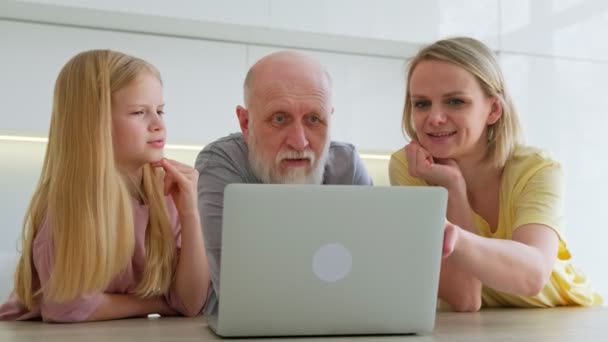 Amistoso tres personas de edad, varias generaciones de la familia utiliza el ordenador portátil juntos, abuelo viejo feliz, madre adulta joven y nieta niña se ríen viendo un programa en línea en el ordenador en casa. — Vídeos de Stock