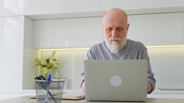 Cute elderly gray-haired grandfather is studying with an online tutor. Teacher talking conference call making video chat learning language taking notes sitting at home office desk looking at laptop. — Stock Video