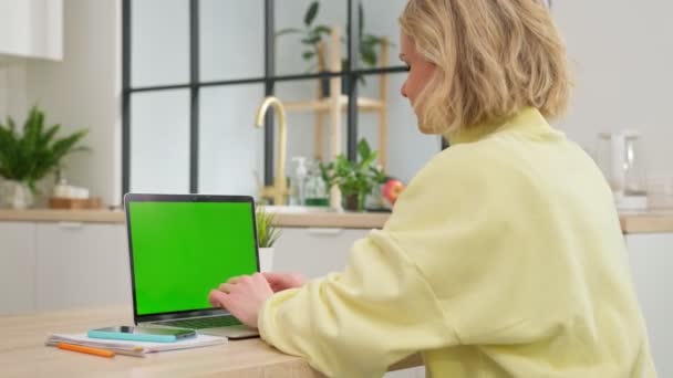 Junge kaukasische Blondine im gelben Pullover arbeitet zu Hause auf einem Laptop mit grünem Chromakey-Bildschirm. Mädchen arbeitet am Laptop, druckt Briefe und arbeitet aus der Ferne. Geschäftsfrau arbeitet im Büro — Stockvideo