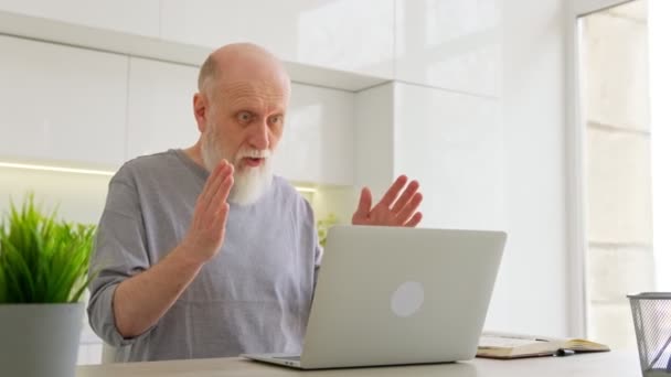Der attraktive ältere Großvater unterhält sich im Videochat mit seinen Enkelkindern, während er zu Hause sitzt, mit einem modernen Laptop. Glücklicher alter Mann mit grauem Bart unterhält sich online mit einem Freund am Laptop. — Stockvideo