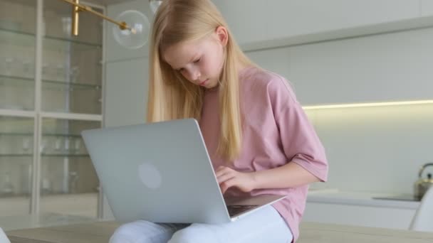 Blonde Kafkasyalı genç kız dizüstü bilgisayarla çalışıyor. Evde, masada oturuyor. Kız arkadaşlarıyla sohbet ediyor, laptopunu izliyor ve evdeki arkadaşlarına mesaj yazıyor.. — Stok video