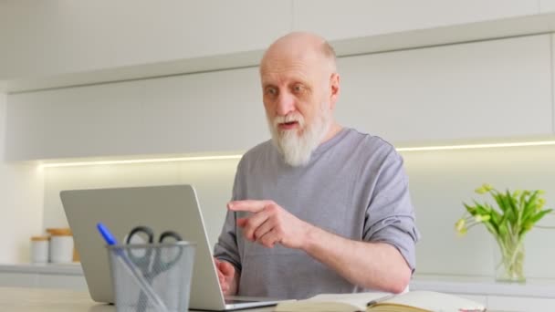 Счастливый старик с седой бородой ведет онлайн-разговор с другом на ноутбуке. Привлекательный дедушка разговаривает в видеочате со своими внуками, используя современный ноутбук, сидя дома. — стоковое видео