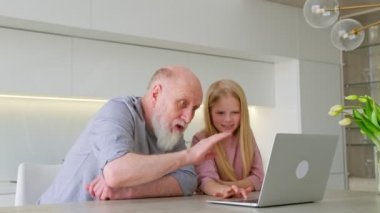 Yaşlı gri saçlı büyükbaba ve torunu bilgisayarın diğer tarafında oturup video bağlantısıyla iletişim kuruyor, gülüyor ve ellerini sallıyorlar. Video aracılığıyla uzak mesafeden aile iletişimi.