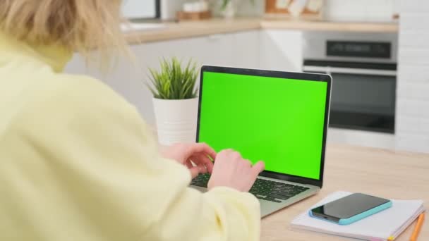 ビジネスの女性は木製の机の上のコンピュータで働き、空白の緑のスクリーンを見る。リモートワークホームに座っている間、空白の緑のラップトップ画面を持つラップトップコンピュータを使用してオフィスの人. — ストック動画