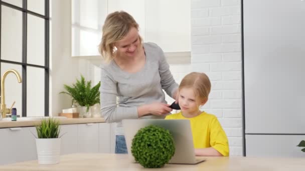 Anne, sevgili kızının saçını tarıyor, sarışın kız bilgisayardaki görüntülü sohbet yoluyla çevrimiçi eğitime hazırlanıyor. Genç blogcu çevrimiçi bir performansa hazırlanıyor ve kendini.... — Stok video