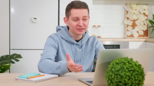 Comunicarse a través de chat de vídeo con la gente a distancia. Entrenamiento en línea. Joven hombre caucásico habla a través de enlace de vídeo con familiares o amigos sentados frente a la computadora portátil en la mesa en casa en la sala de estar. — Vídeo de stock