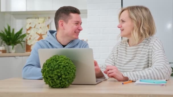 Meisje en man zitten samen aan tafel en gebruiken laptop tijdens een online computerles. Jongeman en schattig meisje werken en communiceren met elkaar samen op laptop terwijl zitten thuis. — Stockvideo