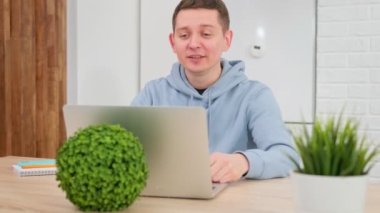 Adam zoom video konferansı yoluyla dizüstü bilgisayarla iletişim kuruyor, elleriyle hareket ediyor ve kameraya konuşuyor. Kafkasyalı genç adam görüntülü konuşma yoluyla iletişim kuruyor, evde uzaktan eğitim alıyor..
