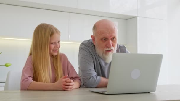 İki kuşak büyük kız torununun büyükbabasıyla eğlenmesi çizgi film izlemesi, bilgisayar ekranını evde izlemesi. Büyükbaba ve küçük torun birlikte masada otururken dizüstü bilgisayar kullanıyorlar. — Stok video