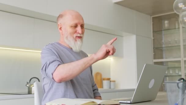 Stary dziadek uśmiecha się i macha rękami do kamery, prowadzi rozmowy z krewnymi. Starszy emeryt komunikuje się ze swoimi wnukami poprzez łącze wideo przez nowoczesny laptop w domu. — Wideo stockowe