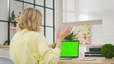 Genç sarışın öğrenci web kamerasında sohbet ediyor, boş yeşil dizüstü bilgisayara bakıyor. Güzel bir kız bilgisayar üzerinden video konferansı düzenler, elleriyle jestler yapar, web kamerasından konuşur..