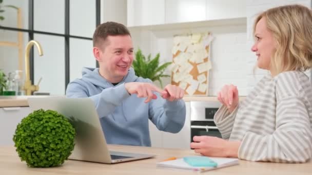 Comunicación entre dos personas sentadas en casa en la sala de estar en la mesa con portátil. Hombre y mujer se sientan juntos, se comunican entre sí, hacen gestos con sus manos, sonríen y ríen. — Vídeos de Stock