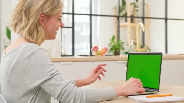 Chica bonita llama a la videoconferencia en el ordenador portátil, gestos con las manos, habla por webcam. Joven estudiante rubia está estudiando en la webcam en el chat en casa, mirando en blanco pantalla verde de la computadora portátil. — Vídeo de stock