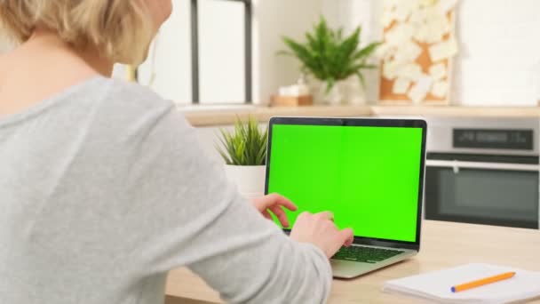 Frau sitzt am Schreibtisch und schaut auf tragbares Computergerät mit leerem grünen Bildschirm zu Hause, das Nachrichten auf Tastatur schreibt. Technik, Chromakey, Vorlage, Layout, Unterhaltungskonzept. Blick nach hinten. — Stockvideo