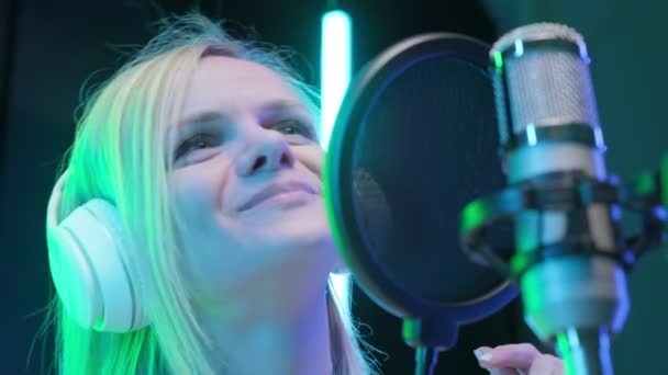 Portrait blonde girl singer in headphones singing song in music recording studio. Caucasian girl records new music track, sings song into microphone. — Stok video