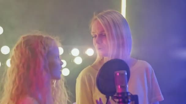 Frau und Mädchen im Tonstudio nehmen Song für neues Album auf. Mutter und Tochter singen im Karaoke-Club in bunten Scheinwerfern ins Mikrofon. Sänger stehen auf der Bühne. — Stockvideo