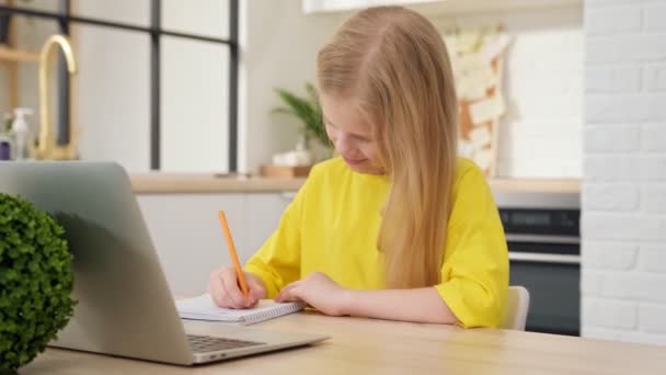 Szőke lány házi feladatot csinál otthon egy laptopon. Online tanulás, távoktatás, otthoni oktatás, iskolai technológia, üzleti konferencia. A gyerekek házi feladatot csinálnak otthon. Vissza az iskolába.. — Stock videók