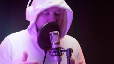 Beyaz sweatshirt ya da kapüşonlu kulaklık takan, profesyonel kayıt stüdyosunda, renkli neon ışıklarla dolu bir mikrofon önünde hip-hop şarkısı kaydeden, traşsız, beyaz tenli rapçi..
