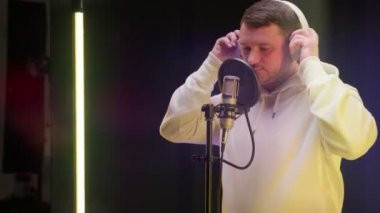 Çekici traşsız sanatçı kulaklık takar ve mikrofona şarkı söyler. Rapçi şarkısını stüdyoda kaydediyor. Hip-hop müzik, ses prodüksiyonu. Profesyonel kayıt stüdyosu, ses kaydı yapan adam..