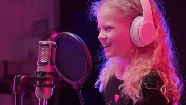 Biała dziewczyna nagrywa nowy utwór muzyczny, śpiewa piosenkę do mikrofonu. Portret młodej blondynki śpiewaczki w słuchawkach śpiewającej piosenkę w studiu nagraniowym. — Wideo stockowe
