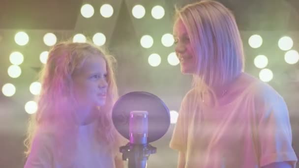 Frau und Mädchen im Tonstudio nehmen Song für neues Album auf. Mutter und Tochter singen im Karaoke-Club in bunten Scheinwerfern ins Mikrofon. Sänger stehen auf der Bühne. — Stockvideo