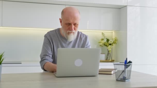 Повільний рух відео милий літній чоловік працює вдома за ноутбуком. Відставний дідусь вчиться використовувати клавіатуру ноутбука і позу, сидячи вдома на робочому місці. Нова технологія для літніх людей . — стокове відео