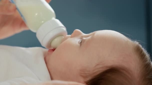 Caucasian newborn baby drinking mothers milk from small plastic baby bottle through pacifier. Portrait toddler drinking diluted milk powder. Concept of motherhood and childhood. Close up footage. — Stock Video