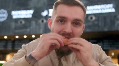 Portresi olmayan traşsız bir adam fast food yer ve etli hamburgeri karbonatlı içecekle yer. Tıraşsız bir adam sığır eti yiyip samandan su içerek açlığını giderir..