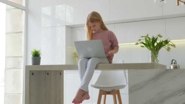 Gros plan d'un étudiant heureux discutant en ligne avec des amis à la maison. Enfant amusant utilisant un ordinateur portable pour l'apprentissage en ligne à l'intérieur. Portrait de fille blonde souriante regardant l'écran d'ordinateur dans le salon. — Video