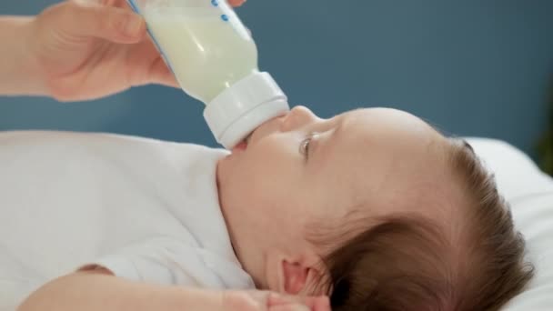 Портрет малыша, пьющего сухое разбавленное молоко. Понятие материнства и детства. Кавказский новорожденный ребенок пьет молоко матерей из маленькой пластиковой бутылочки младенца через соску. Закрыть съемку. — стоковое видео