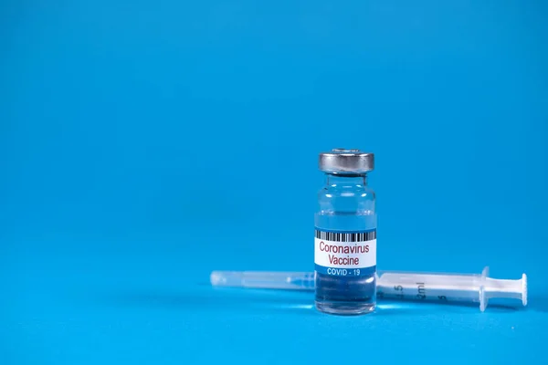 Concept of victory over epidemic of Sars-nCoV-2. Virus 2019-nCoV defeated. Invented coronavirus covid-19 vaccine in glass medicine bottle, syringe for injection on blue background with space for text