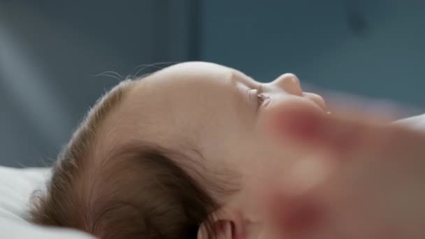 Close-up retrato de amorosa jovem mulher caucasiana, mãe curva a cabeça para o bebê recém-nascido de dois meses de idade, beija-o suavemente na bochecha. Relacionamento mãe-filho, cuidado da criança, família amorosa. — Vídeo de Stock