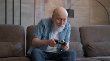 Kır saçlı emekli, koltukta oturan, duygusal olarak konsolda oynayan, oyunu kaybeden, mağlubiyet duygularını kaybeden. Zafer sevinci ile kablosuz kontrolörle video oyunu oynayan yaşlı bir adamın portresi.