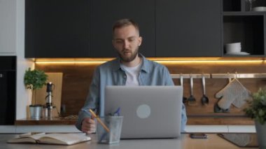 Öğrenci internet öğretmeninden öğrenir, konuşur ve not defterine yazı yazar. Tıraşsız erkek serbest çalışıyor. Evde dizüstü bilgisayarının başında oturuyor. Web kamerasıyla görüntülü sohbet yoluyla iletişim kuruyor..