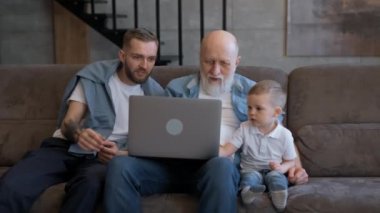 Mutlu aile, yaşlı dedesi ve tatlı çocuğu olan bir baba dizüstü bilgisayar ekranına bakıyor sosyal ağlarda eğlenceli videolar izleyerek evde kanepede dinleniyor..