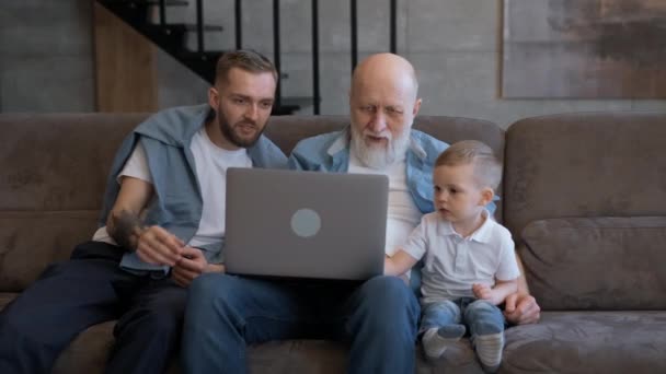 Szczęśliwa rodzina, ojciec ze starszym dziadkiem i słodkie dziecko za pomocą laptopa patrzy na ekranie komputera korzystających oglądając śmieszne filmy na portalach społecznościowych zakupy online relaks na kanapie w domu razem. — Wideo stockowe