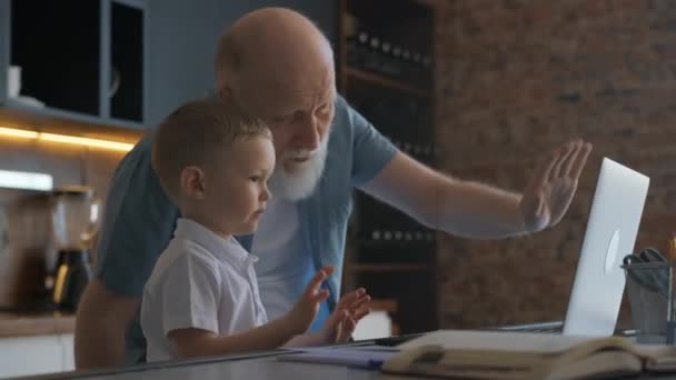 Netter Junge und Großvater kommunizieren im Videochat mit Mutter und Vater, lächeln und winken der Familie zu. Glückliche Beziehung in der Familie mit älteren Menschen, zu Hause am Tisch sitzen. — Stockvideo