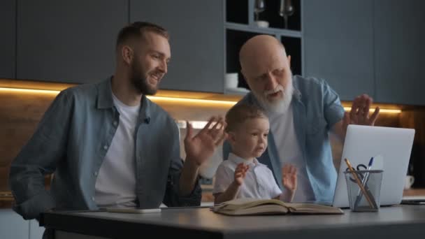 Familia feliz, padre con abuelo anciano y lindo niño usando el ordenador portátil, mirando la pantalla de la computadora saludando las manos comunicándose con los familiares a través de chat de vídeo. — Vídeo de stock