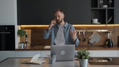 Genç serbest çalışan adam gergin bir şekilde mutfakta dolaşıyor ve telefonla konuşuyor, elleriyle duygusal dalgalar ve jestler yapıyor, dizüstü bilgisayarında bilgi arıyor ve evdeki defterine düşüncelerini yazıyor..