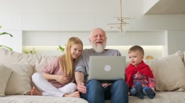 Nesiller boyu mutlu bir aile, torunları olan yaşlı gri saçlı bir büyükbaba, erkek ve kız, evinde bilgisayar başında oturmuş, komik videolar izliyor ve neşeyle gülüyorlar..