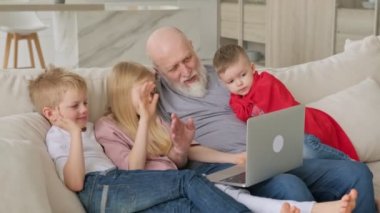 Mutlu aile nesilleri, iki torunu ve iki torunu olan yaşlı gri saçlı bir büyükbaba, görüntülü sohbet zoom ile iletişim kurarken web kameralarına el sallıyor..