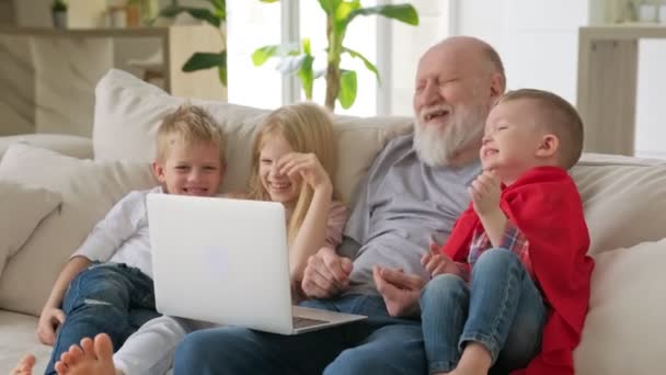 Glückliche Familiengenerationen, ein älterer, grauhaariger Großvater mit zwei Enkelkindern und Enkelin, winken mit den Händen zur Begrüßung in die Webcam, während sie per Videochat-Zoom kommunizieren.. — Stockvideo