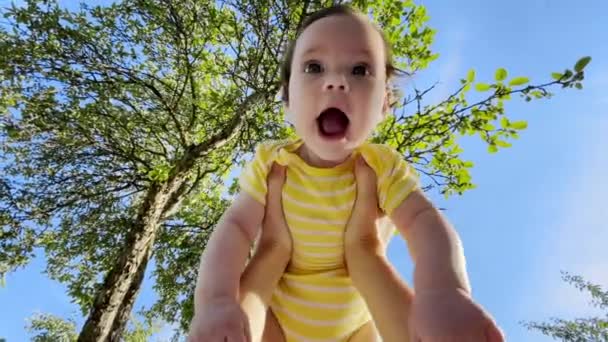 POV shot mother held small happy smile cute child on arm length above him, playing together in nature with trees and blue sunny sky background, filmed first person, carefree family enjoys weekend. — Stok Video